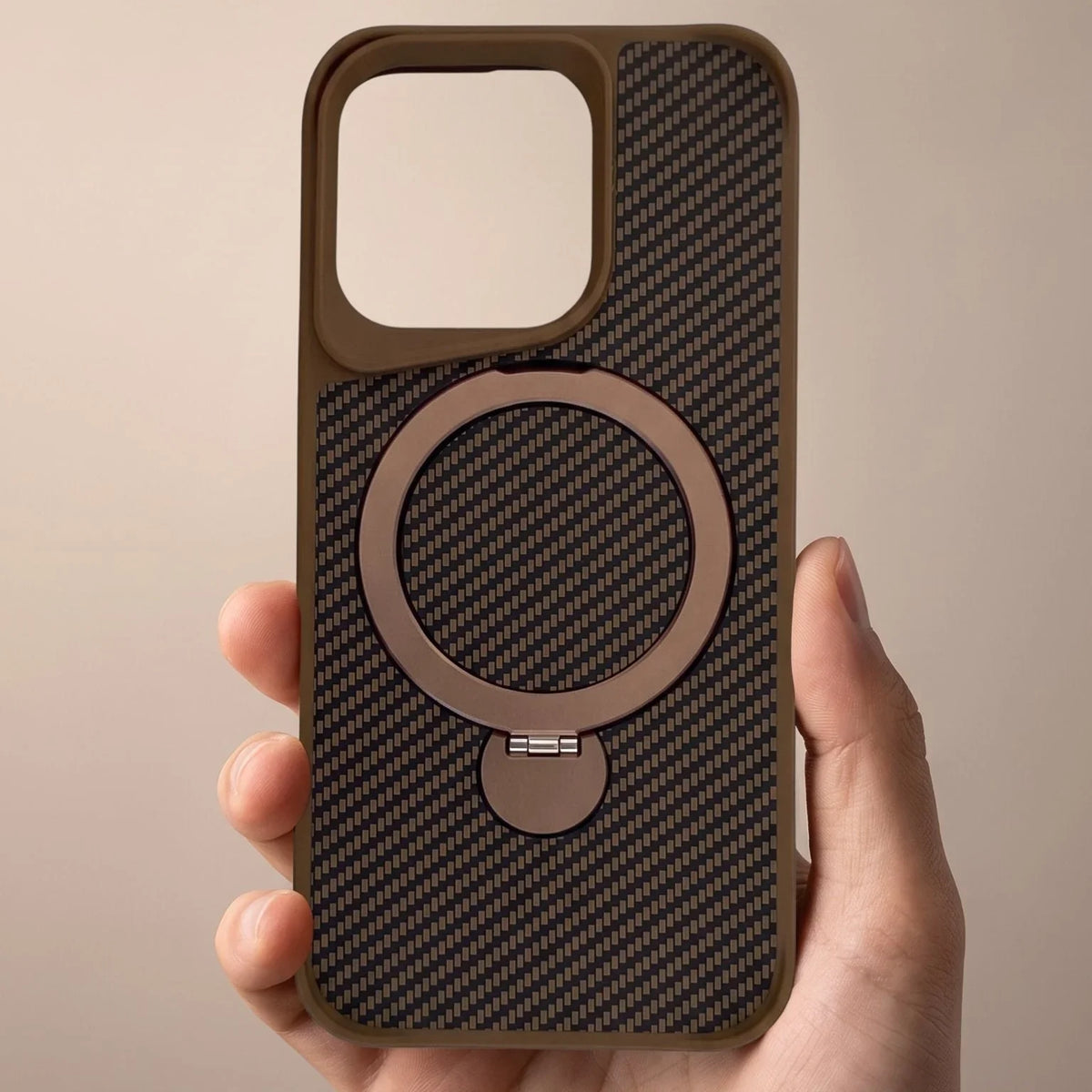 Hand holding a brown carbon fiber MagSafe iPhone case with a built-in ring stand